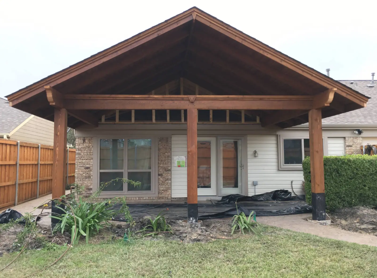 Finished gabled patio cover with stained cedar posts on a brick home
