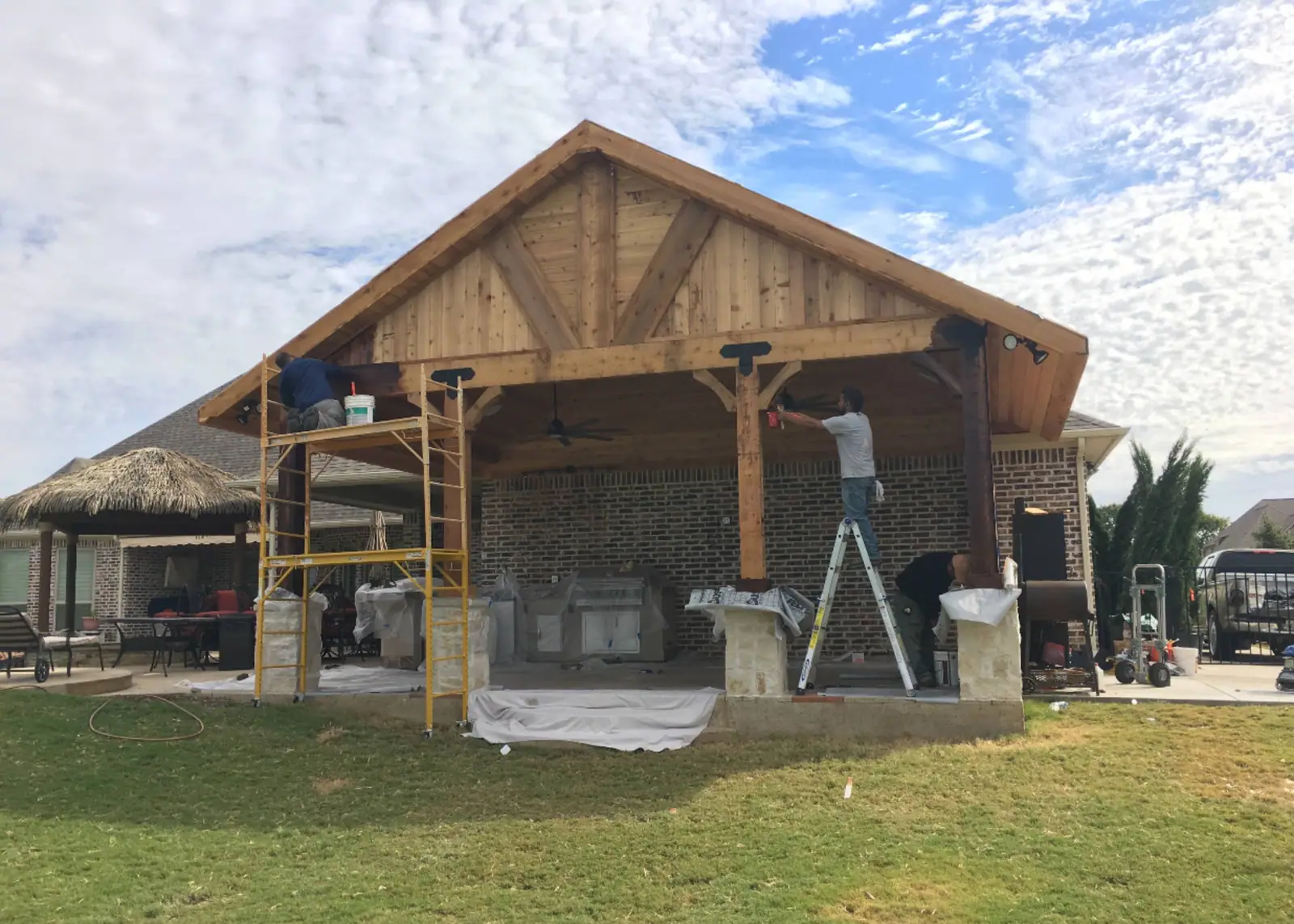 Cedar patio cover framing with stone column bases going up behind a home