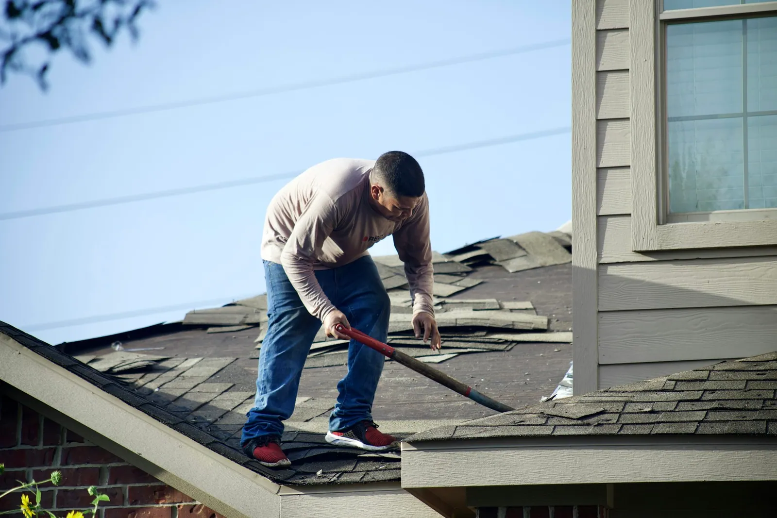 Roofer tearing off damaged shingles