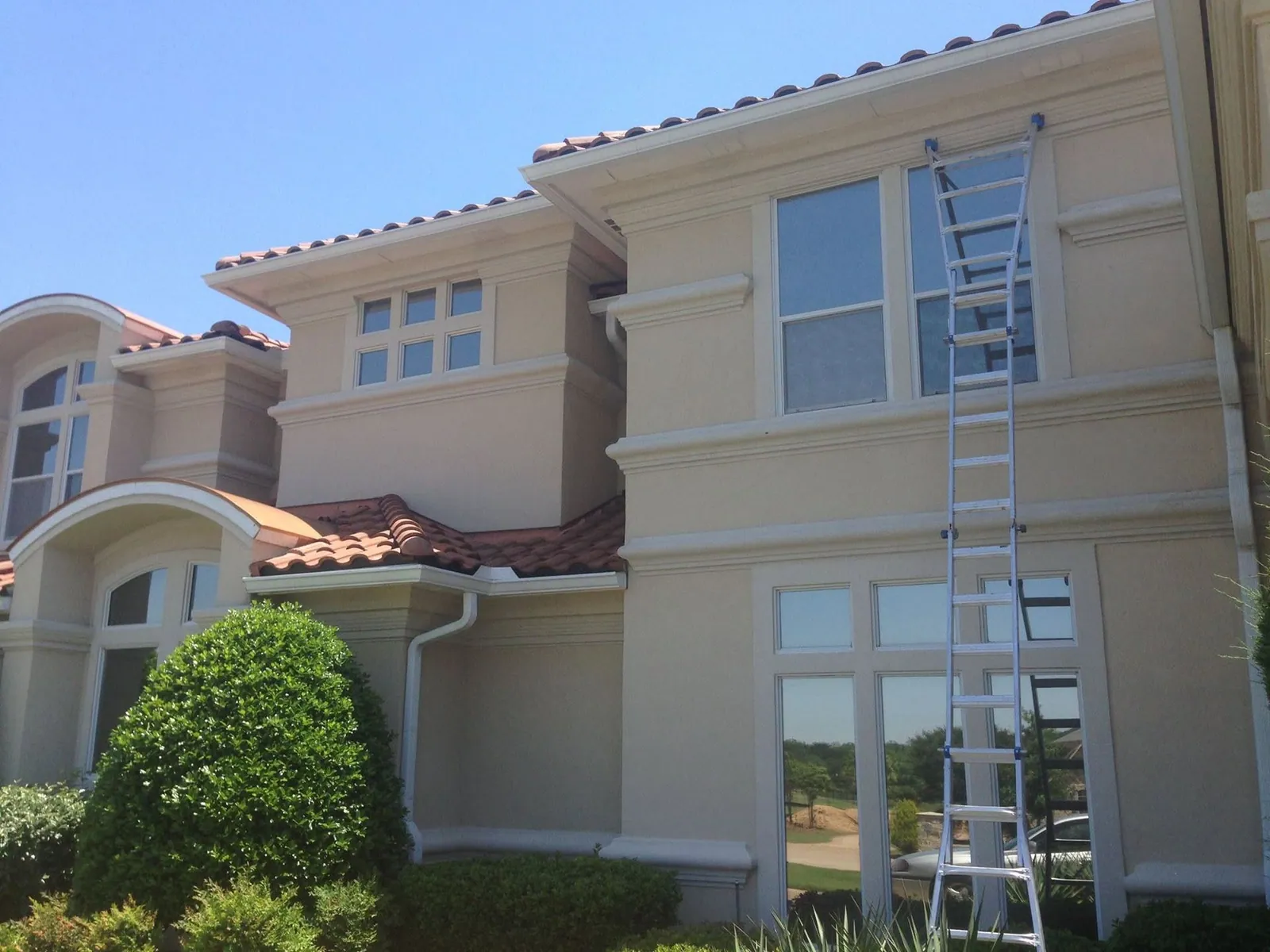 Crew member on a ladder working on a two-story stucco home