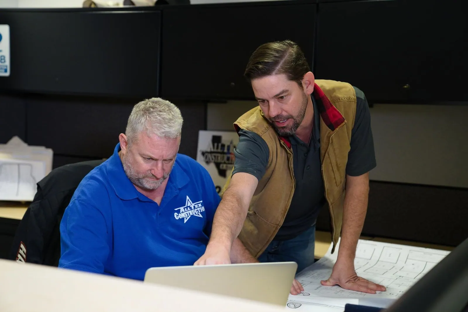 Two AllTex team members reviewing plans on a laptop at a desk